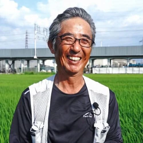水田を背に笑う渡邊勝彦。